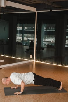 An athletic young man does exercises in the fitness room. A professional guy does yoga in the gym.