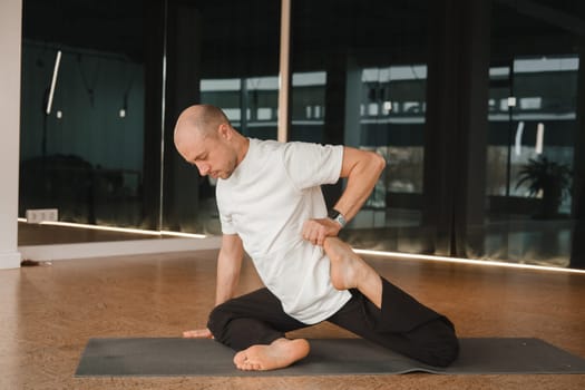 An athletic young man does exercises in the fitness room. A professional guy does yoga in the gym.