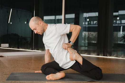 An athletic young man does exercises in the fitness room. A professional guy does yoga in the gym.