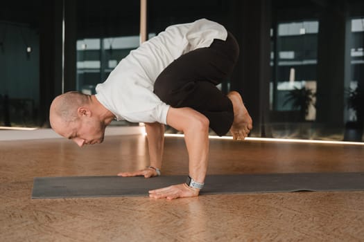 An athletic young man does exercises in the fitness room. A professional guy does yoga in the gym.