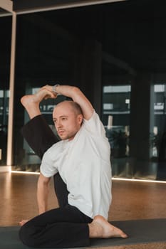 An athletic young man does exercises in the fitness room. A professional guy does yoga in the gym.