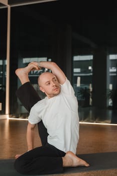 An athletic young man does exercises in the fitness room. A professional guy does yoga in the gym.