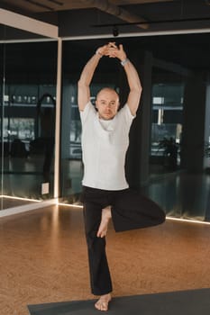 An athletic young man does exercises in the fitness room. A professional guy does yoga in the gym.