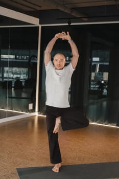 An athletic young man does exercises in the fitness room. A professional guy does yoga in the gym.