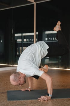 An athletic young man does exercises in the fitness room. A professional guy does yoga in the gym.