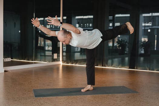 An athletic young man does exercises in the fitness room. A professional guy does yoga in the gym.