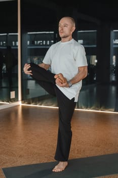 An athletic young man does exercises in the fitness room. A professional guy does yoga in the gym.