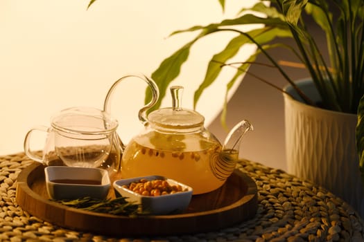 A teapot with sea buckthorn tea, honey and a plate with sea buckthorn on a tray.