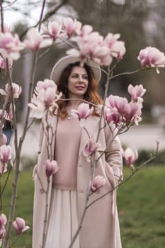 Woman magnolia flowers, surrounded by blossoming trees, hair down, white hat, wearing a light coat. Captured during spring, showcasing natural beauty and seasonal change