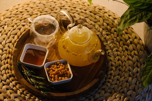 A teapot with sea buckthorn tea, honey and a plate with sea buckthorn on a tray.