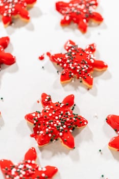 Vivid red star-shaped cookies, generously iced and speckled with green and white holiday sprinkles, freshly prepared and laid out to dry.