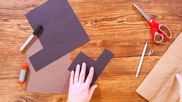 Step by step. Flat lay. Teacher guides online class through making a paper puppet from a brown bag, creatively using a wooden surface as a workspace.