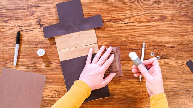 Step by step. Flat lay. Teacher guides online class through making a paper puppet from a brown bag, creatively using a wooden surface as a workspace.