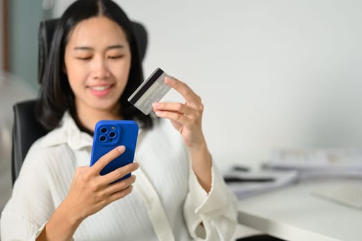 Happy young woman holding credit card making online payment or ordering via the internet on smartphone.