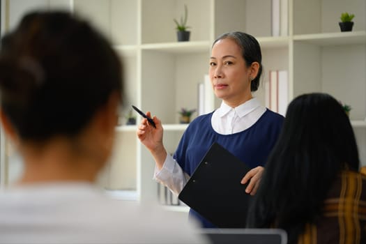 Senior female lecturer gesturing while explaining something in class.