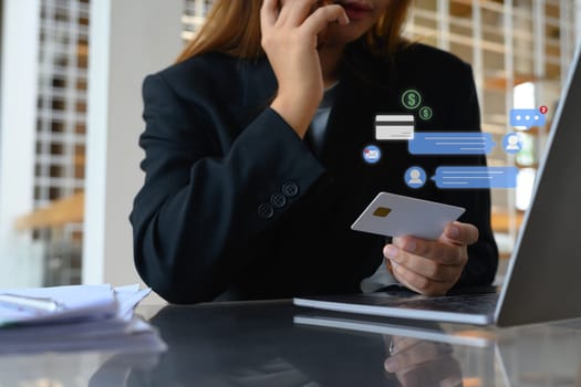 Businesswoman with a credit card in hand talking on mobile phone at her office desk.