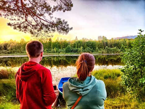 Tourist Couple Enjoying a Lakeside Sunset in Nature. A couple watches the sunset by tranquil lake, surrounded by trees