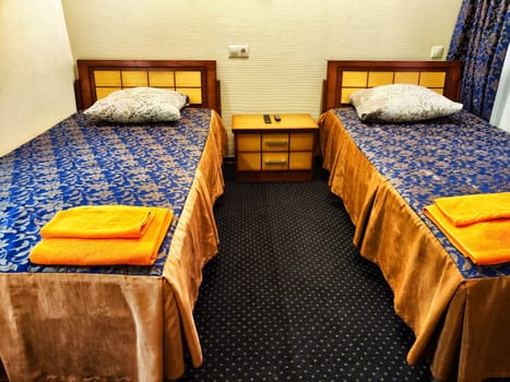 Twin Beds in Cozy Hotel Room. Two single beds with blue bedding and orange towels in a hotel room