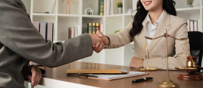 A lawyer and a businesswoman shake hands and reach an agreement on a cooperation contract document. In the lawyer's office and there is a hammer lying on the table..