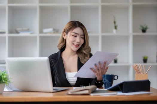 Beautiful accountant sitting working with laptop calculating financial and tax figures for company on desk in living room..