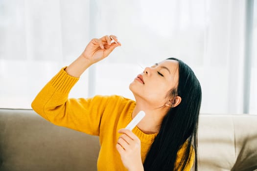 Highlighting COVID-19 self-test, Asian woman uses a rapid antigen test kit at home inserting a swab into her nose. Depicting virus prevention and pandemic protection measures.