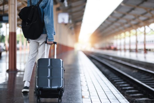 A young man holding a suitcase waits for a train at the train station for traveling..