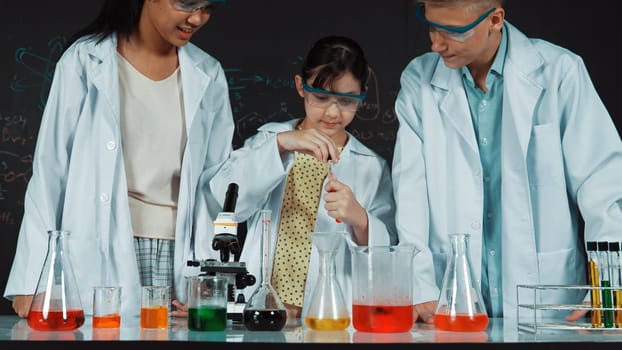 Smart girl pour colored solution in to beaker while diverse student excited about doing experiment. Professional scientist prepare for doing experiment at blackboard with chemical theory. Edification.