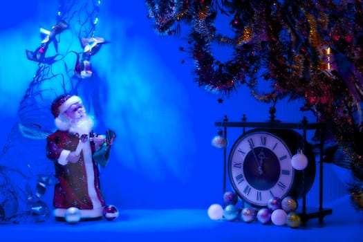 the annual Christian festival celebrating Christ's birth, held on December 25 in the Western Church. Santa Claus in blue light and vintage clock. New Year's Christmas toys,garlands.