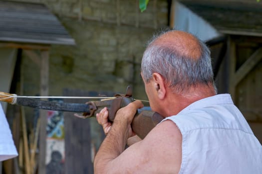 a medieval bow of a kind that is fixed across a wooden support and has a groove for the bolt and a mechanism for drawing and releasing the string. Traveling pensioner shoots a crossbow in a fortress