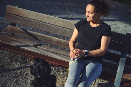 Portrait of a beautiful smiling athletic woman sitting on a bench, relaxing and walking her cocker spaniel dog on leash. Pets concept. People. Domestic animals, Healthy and active lifestyle concept