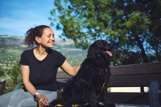 Happy middle aged woman and her cocker spaniel god looking way, sitting on the bench against mountains nature background. Woman walking pet in the nature