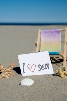 I LOVE SEA text on paper greeting card on background of beach chair lounge starfish summer vacation decor. Sandy beach sun coast. Holiday concept postcard. Travel Business concept