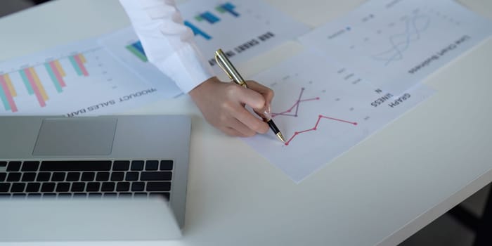 Finance concept. Close up businesswoman hold a graph pen and writing report, and memo, and analyzing business documents with a laptop computer.