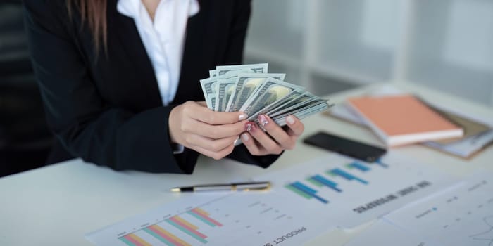 Businesswoman or financial bookkeeper holding bundle of money dollar for payment salary and income. entrepreneur counting money cash count salary profit finance at office.
