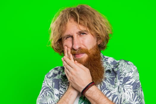 Dental problems. Young man touching cheek, closing eyes with expression of terrible suffer from painful toothache, sensitive teeth, cavities. Handsome redhead guy isolated on chroma key background