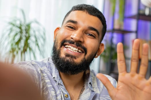 POV view of Indian young man blogger taking selfie on smartphone communicating video call online with subscribers recording stories for social media. Bearded Arabian guy holding mobile phone with hand
