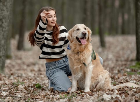 Teenage Girl Sits With Golden Retriever In Park During Autumn