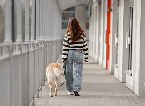 Teen Girl With Golden Retriever Sits In City During Spring, Viewed From Behind