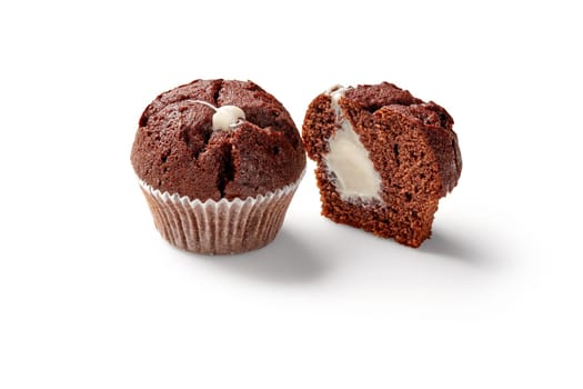 Delicious whole and sliced soft airy chocolate muffins in baking paper cups with delicate creamy filling, isolated on white background