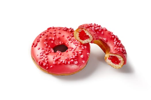 Vibrant red glazed soft donuts with sweet and sour berry jelly filling sprinkled with sugared berry crumbs, isolated on white background. Handcrafted confectionery