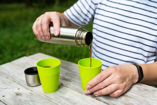 A man on the street pours coffee from a thermos into a green cup, enjoying his outdoor recreation