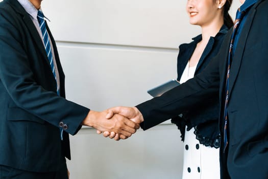 Business people agreement concept. Businessman do handshake with another businessman in the office meeting room. Young Asian secretary lady stands beside them. uds