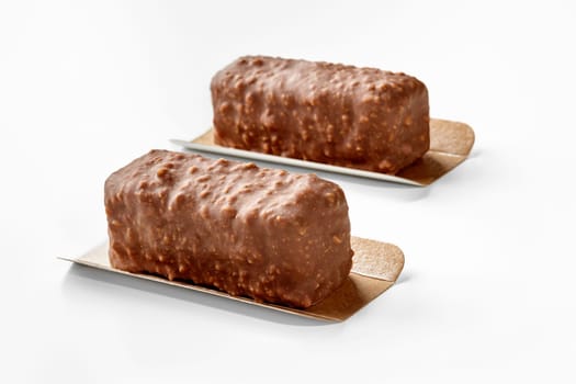 Two appetizing nuts and chocolate covered ice cream bars presented on golden serving cardboards on white background, perfect for sweet treat