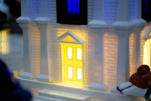 Prototype printed on 3D printer brick building with columns and glowing windows. Model of building with white and brown color, windows with light shining, created by 3D printer from molten plastic