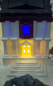 Prototype printed on 3D printer brick building with columns and glowing windows. Model of building with white and brown color, windows with light shining, created by 3D printer from molten plastic