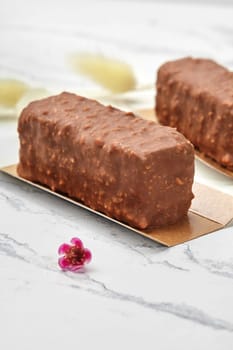Appetizing textured chocolate nut loaf cakes elegantly presented on golden cardboards on marble backdrop with delicate flower accent. Traditions of confectionery art