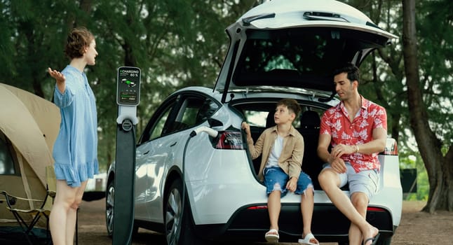 Outdoor adventure and family vacation camping in nature travel by eco friendly car for sustainable future. Lovely family recharge EV car with EV charging station in campsite. Perpetual