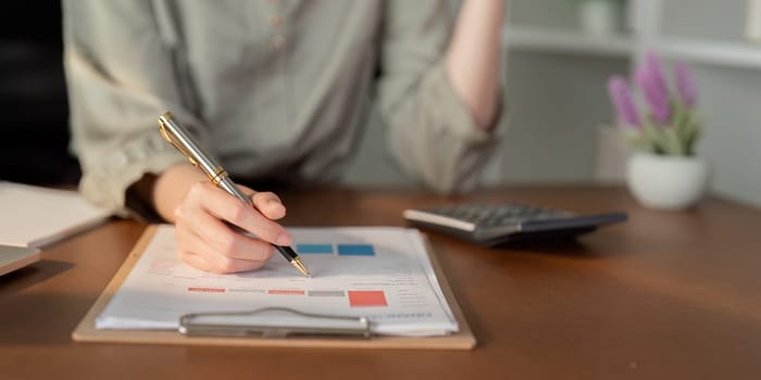 Businesswoman using laptop computer and working at office with calculator document on desk, doing planning analyzing the financial report, business plan investment, finance analysis concept.