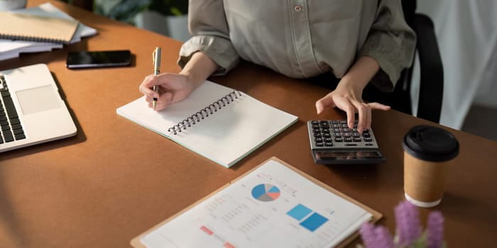 Businesswoman using laptop computer and working at office with calculator document on desk, doing planning analyzing the financial report, business plan investment, finance analysis concept.