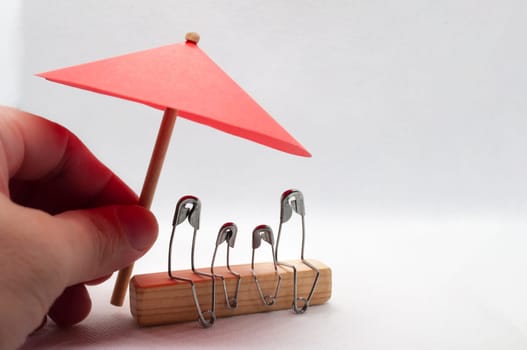 Model safety pin of family sitting on wooden block with red umbrella background. Insurance concept.